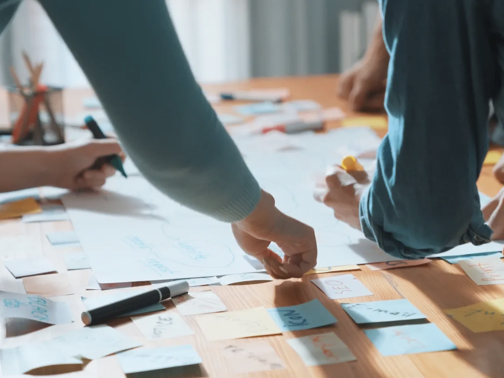 Hands arranging sticky notes and notes on a table during a planning session.